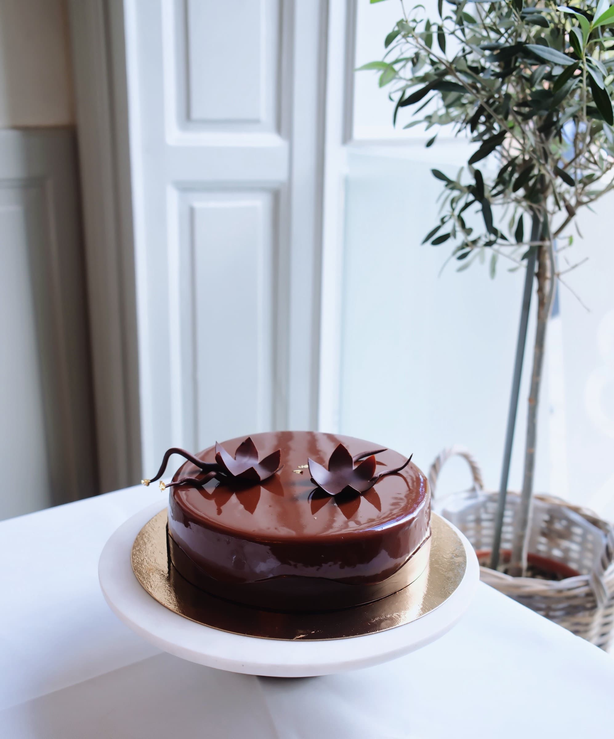 Chokladglaserad tårta med skulpterade chokladblommor, olivträd i bakgrunden