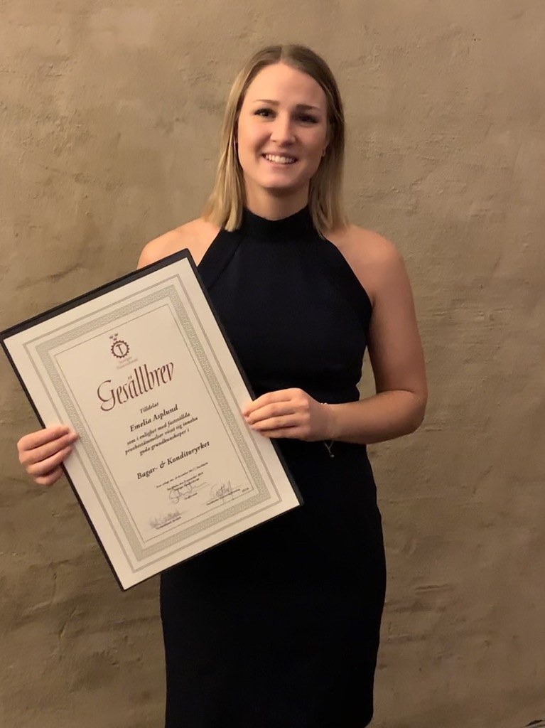 Emelia Asplund med sitt gesällbrev, där det står "Bagar- & Konditoryrket"